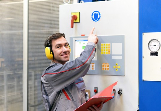 ein Mitarbeiter mit Gehörschutz zeigt auf ein Hinweisschild