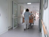 Zwei Personen schieben ein Krankenhausbett durch eine Tür.