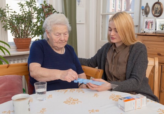 eine Pflegerin hilft einer Patientin bei der Einnahme von Medikamenten