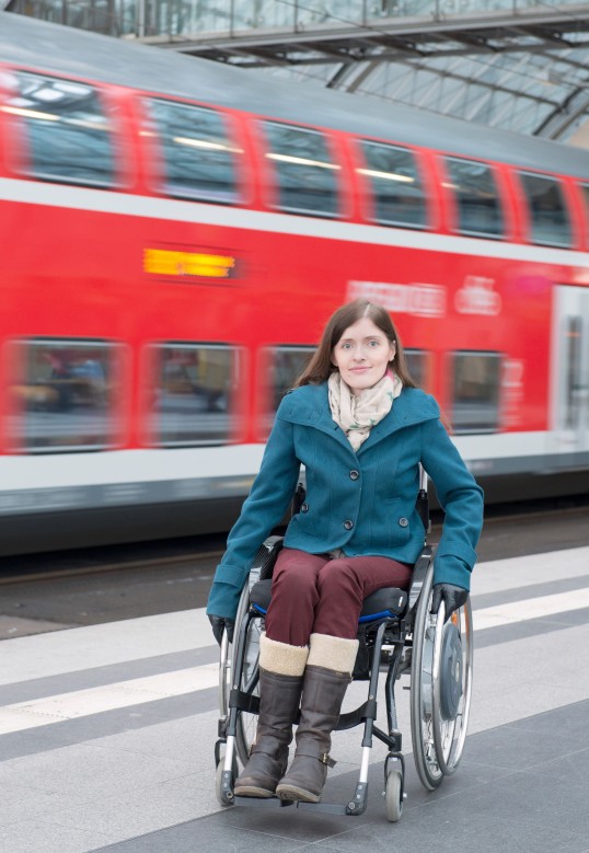 hinter einer Frau, die im Rollstuhl sitzt, fährt ein Zug vorbei
