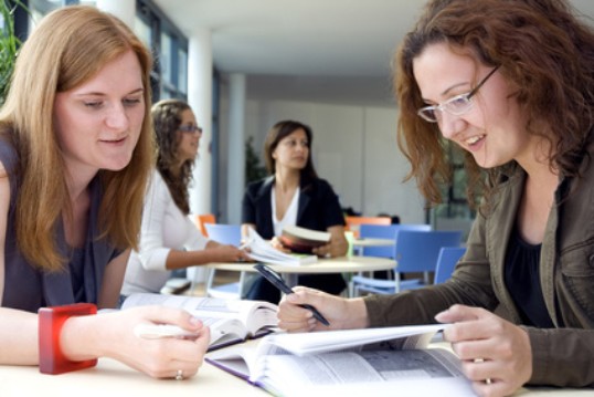 zwei Frauen sitzen an einem Tisch und schauen in Unterlagen