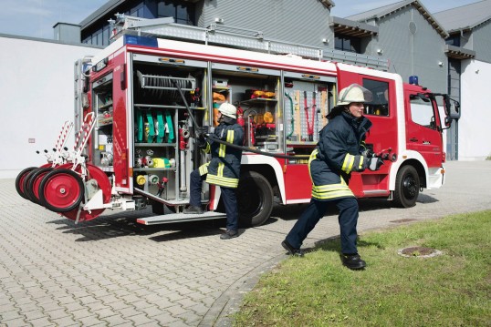 zwei Feuerwehrleute ziehen einen Löschschlauch vom Feuerwehr-Fahrzeug