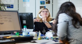 Zwei Frauen sitzen sich an ihren Schreibtischen in einem Büro gegenüber.