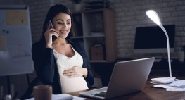 Eine schwangere Frau sitzt in einem abgedunkeltem Raum vor ihrem PC