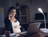 Eine schwangere Frau sitzt in einem abgedunkeltem Raum vor ihrem PC