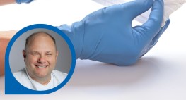 Zwei Hände halten eine Maske, im Vordergrund ist Dr. I. Hosbach