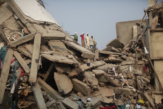 Die eingestürzte Textilfabrik Rana Plaza. Menschen stehen auf den Trümmern.
