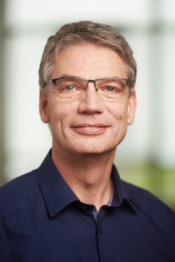 Das Bild zeigt ein Portrait von Professor Windemuth. Er trägt eine Brille und ein dunkelblaues Hemd und lächelt in die Kamera. 