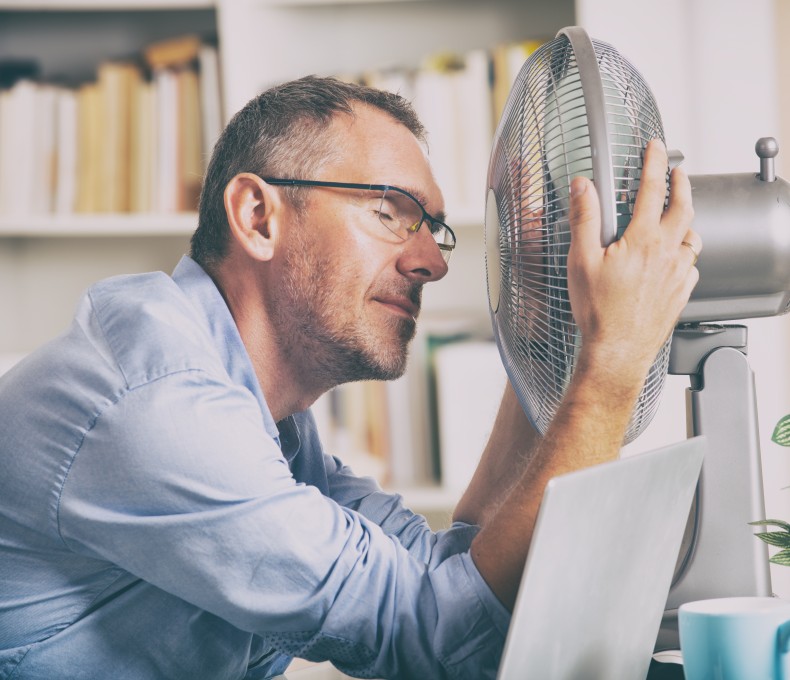 Mann sitzt im Büro vor einem Ventilator. Er hat die Augen zu und wirkt erschöpft. Mann sitzt im Büro vor einem Ventilator. Er hat die Augen zu und wirkt erschöpft.