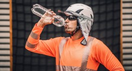 Person mit orangefarbener PSA, die aus einer Wasserflasche trinkt.