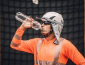 Person mit orangefarbener PSA, die aus einer Wasserflasche trinkt.