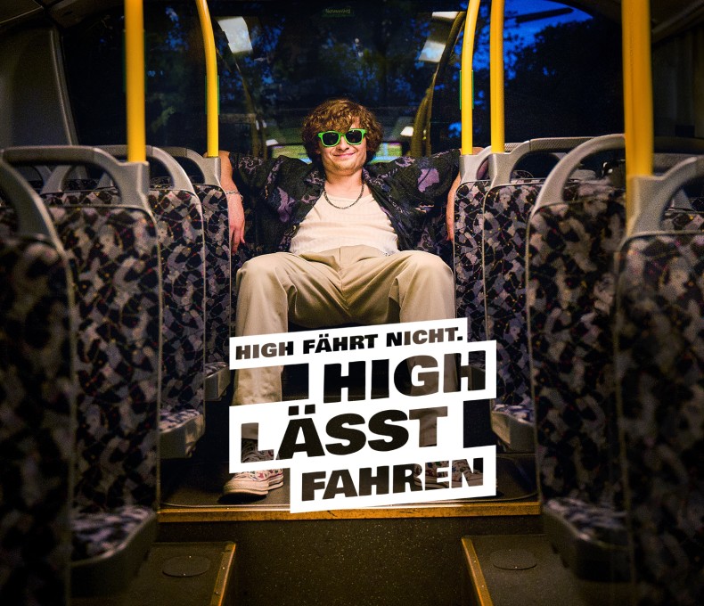 Das Bild zeigt einen jungen Mann mit lockigem Haar und grüner Sonnenbrille, der lässig auf einem Sitz in einem fast leeren Bus sitzt. Seine Arme sind entspannt über die Rückenlehnen der Sitze gelegt. Er trägt eine helle Hose, ein weißes T-Shirt und ein dunkles Hemd mit Muster. Im Vordergrund steht der Text „HIGH FÄHRT NICHT. HIGH LÄSST FAHREN.“ auf weißen, leicht schräg angeordneten Blöcken. Die Innenausstattung des Busses ist mit gemusterten Polstern gestaltet, und das Bild vermittelt eine entspannte, abendliche Atmosphäre. Das Bild zeigt einen jungen Mann mit lockigem Haar und grüner Sonnenbrille, der lässig auf einem Sitz in einem fast leeren Bus sitzt. Seine Arme sind entspannt über die Rückenlehnen der Sitze gelegt. Er trägt eine helle Hose, ein weißes T-Shirt und ein dunkles Hemd mit Muster. Im Vordergrund steht der Text „HIGH FÄHRT NICHT. HIGH LÄSST FAHREN.“ auf weißen, leicht schräg angeordneten Blöcken. Die Innenausstattung des Busses ist mit gemusterten Polstern gestaltet, und das Bild vermittelt eine entspannte, abendliche Atmosphäre.