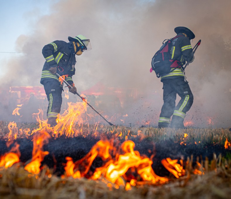Feuerwehrkraft in Schutzkleidung löschen einen Flächenbrand. (Bild: xsim7x / stock.adobe.com)